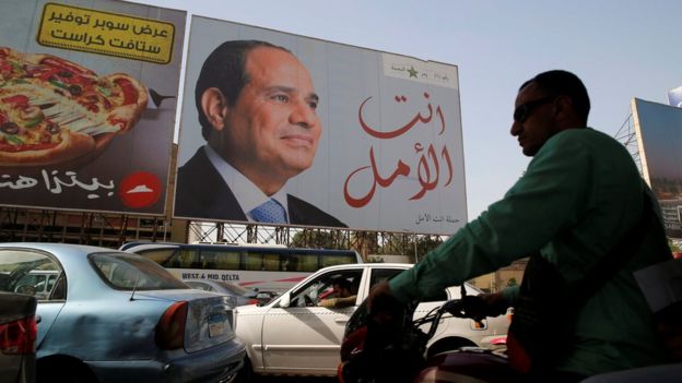 People walk in front of banners with Egypt's President Abdel Fattah al-Sisi during preparations for the presidential election in Cairo, Egypt, 25 March