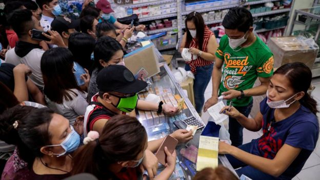 Gente comprando mascarillas en una farmacia en Manila.