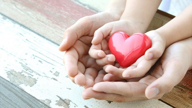 Las manos de un adulto y un un niño sosteniendo la figura de un corazón.