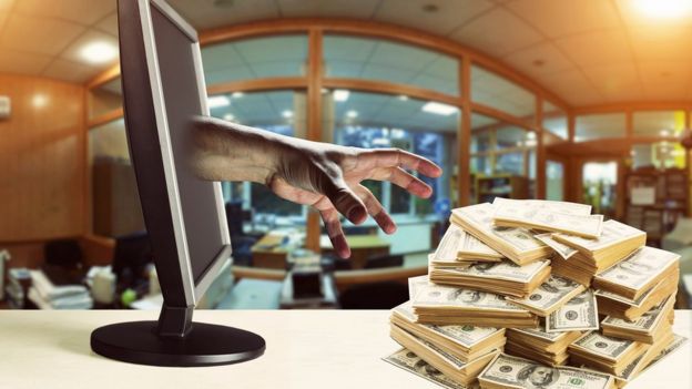 Mano saliendo de la pantalla de una computadora para agarrar un fajo de billetes.