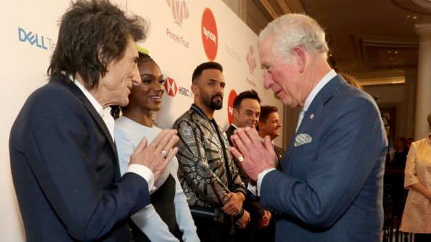 Prince Charles, Prince of Wales uses a Namaste gesture to greet Rolling Stone Ronnie Wood as he attends the Prince's Trust And TK Maxx
