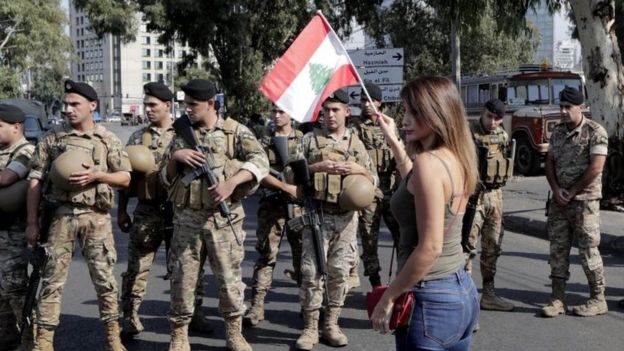 A woman waves a Lebanese flag in front of soldiers in Tripoli, Lebanon. Photo: 22 October 2019