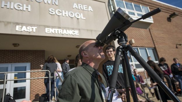 Un hombre observa el tránsito de Mercurio en 2016 con binoculares que tiene un filtro solar antepuesto al objetivo