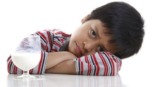 Menino com cra de triste na frente de copo com leite