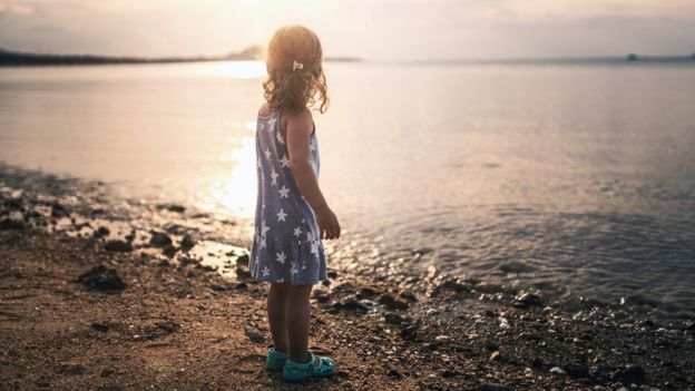 Una niña mira hacia el mar