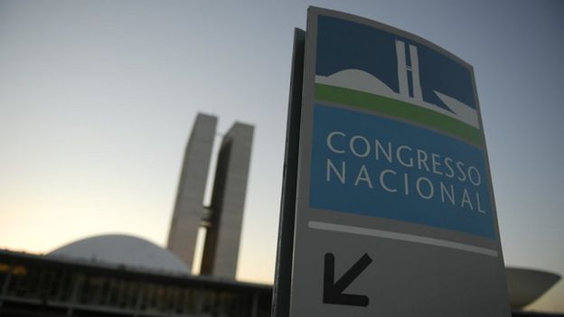 Placa diz "Congresso Nacional", atrás da qual aparecem os prédios do Legislativo em Brasília