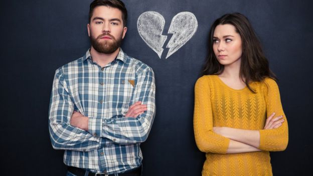 Hombre y mujer mirando la cámara. En la pared dibujado hay un corazón partido.