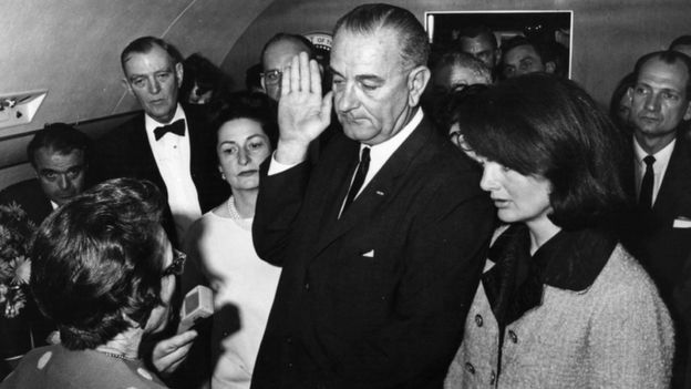 لیندن جانسون در حالی که ژاکلین کندی، در سمت چپ او ایستاده، داخل هواپیمای برگشت از دالاس و با همان انجیل جان اف کندی، به عنوان رئیس‎جمهور جدید سوگند یاد کرد