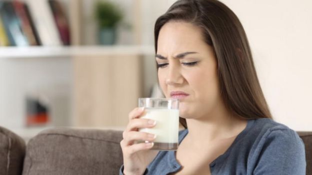 Una mujer huele con asco un vaso de leche.