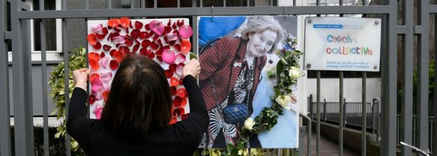 A woman places a picture and tributes to Mireille Knoll on the fence surrounding her building in Paris on March 27