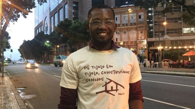 Em rua do Rio de Janeiro, Jac-Ssone Alerte posa para foto sorrindo e exibindo camisa com os dizeres 'De tijolog em tijolo, construímos sonhos'