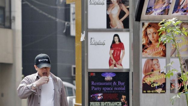 Un hombre pasa por anuncios de clubes con fotos de mujeres.