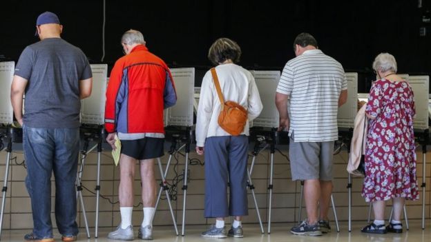 Votantes de espaldas emitiendo su voto.