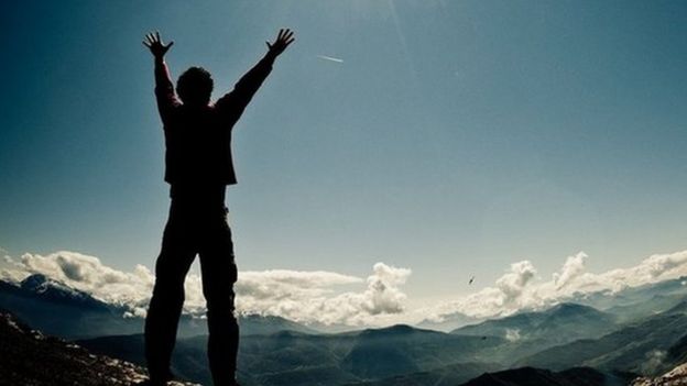 Man on top of a mountain, arms raised, sun rising