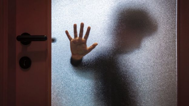 Un niño apoya la mano detrás del vidrio de una puerta.
