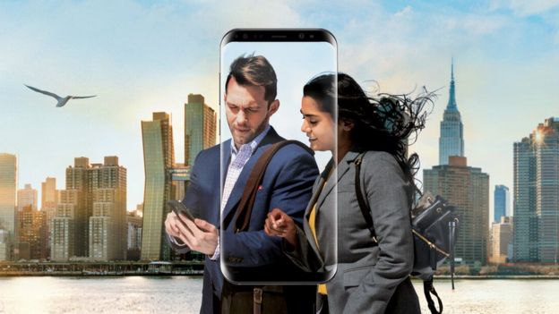 pareja usando un teléfono Samsung con rascacielos en el fondo.