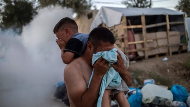 A refugee holds a boy and protects himself from tear gas fired by police at the Moria camp. Photo: 29 September 2019