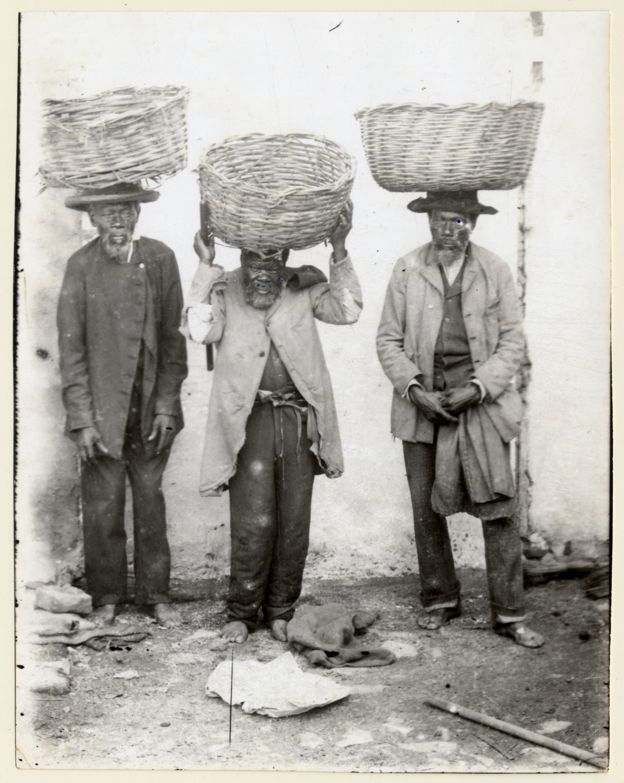 Imagem mostra três homens, ex-escravos, com cestos equilibrados na cabeça. Eles trabalhavam como vendedores ambulantes em Porto Alegre, no final do século 19. Crédito: Acervo do Museu de Porto Alegre Joaquim Felizardo/Autor Desconhecido