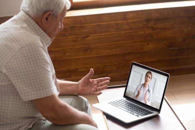 Un hombre frente a una computadora portátil con un médico