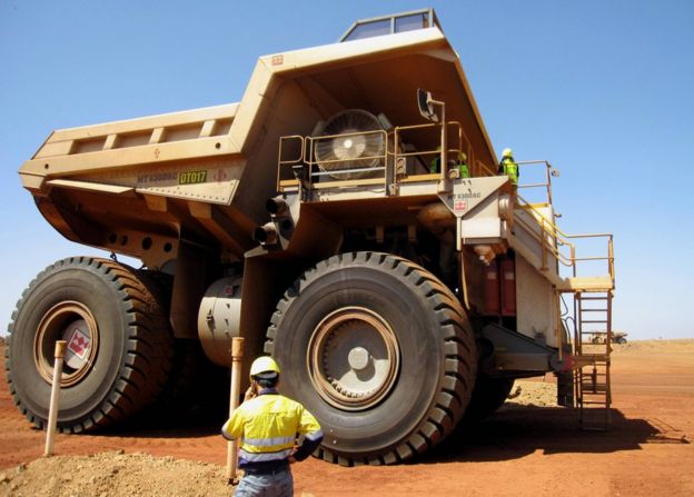 A worker stands before an iron ore tipper truck
