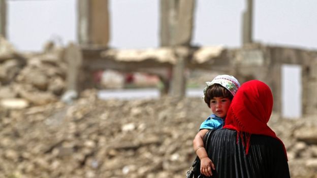 سيدة عراقية تسير رفقة ابنتها قرب مبان مدمرة بسبب القتال جنوب الموصل