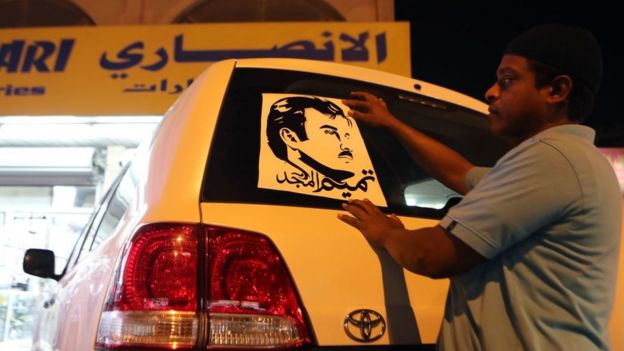 Bir Katar vatandaşı Katar Emiri Temim bin Hamad es-Sani'nin illüstrasyonunu arabasına asıyor