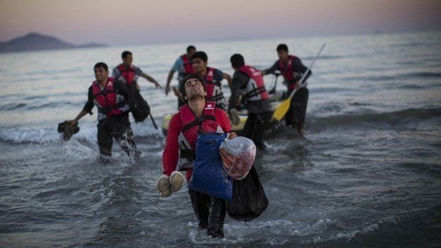 Migrants leaving a dinghy and walking on to a beach in Kos, Greece
