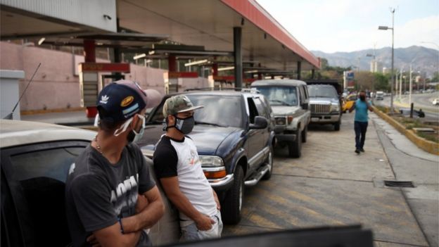 People wearing protective masks stand beside vehicles in line at a fuel station during the nationwide quarantine in response to the spread of coronavirus disease (COVID-19) in Caracas, Venezuela 30 March 2020