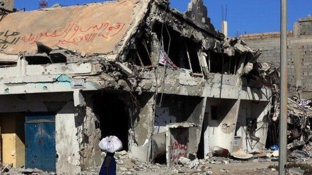 A Libyan woman walks past the rubble of a building in the Mediterranean city of Sirte on 13 October 2012