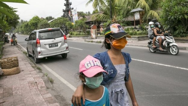 Two children walk through town of Karangasem in Bali wearing breathing masks