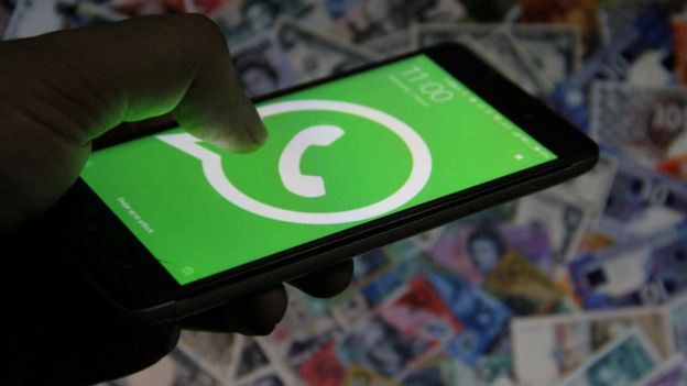 Imagen de una mano usando un celular con el logo de WhatsApp.