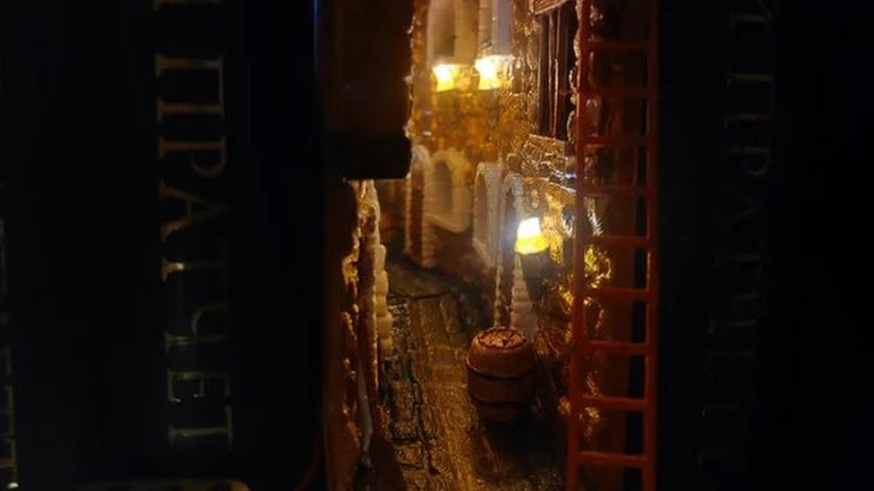 Un primer plano del booknook de Konstatin, que muestra el callejón. En la parte posterior hay un pequeño espejo que refleja el resto del callejón y crea la ilusión de profundidad.