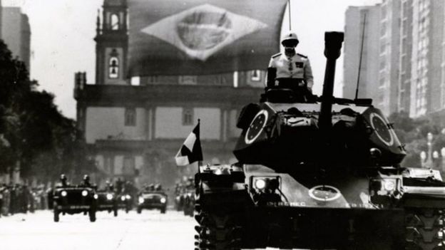 Foto em preto e branco mostra tanque na rua com militar em cima