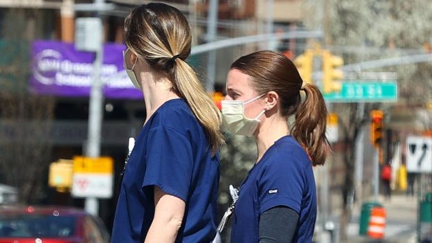 Two nurses wearing masks cross a street in New York City, 27 March 2020