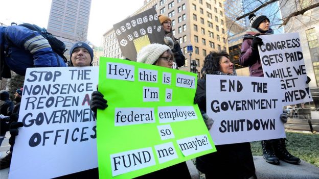 Demonstrators hold signs during a protest rally by government workers and concerned citizens against the government shutdown