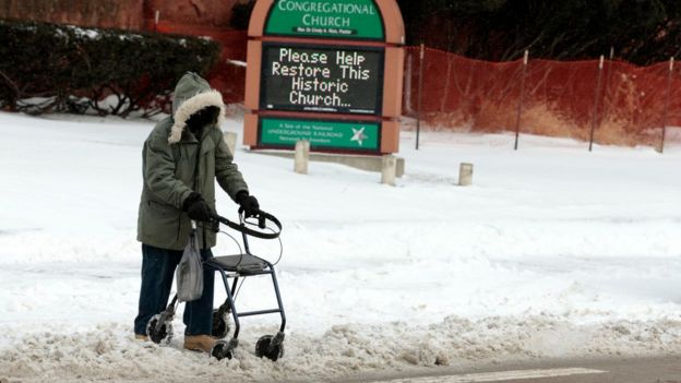 Homem agasalhado anda sobre a neve com a ajuda de um carrinho, em Michigan