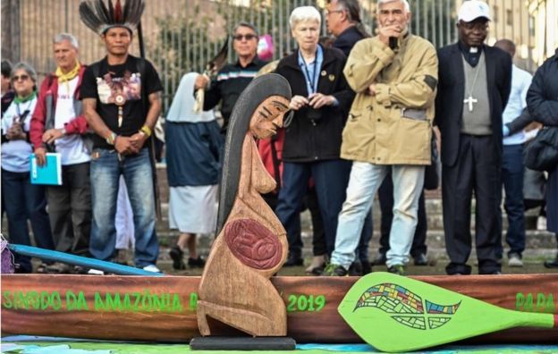 Una escultura de madera tallada de una mujer embarazada y un modelo de piragua