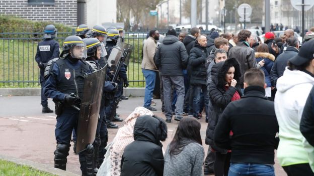 French anti riot police officers (L) stand guard as people gather during a protest on 6 February 2017 in Aulnay-sous-Bois, northern Paris