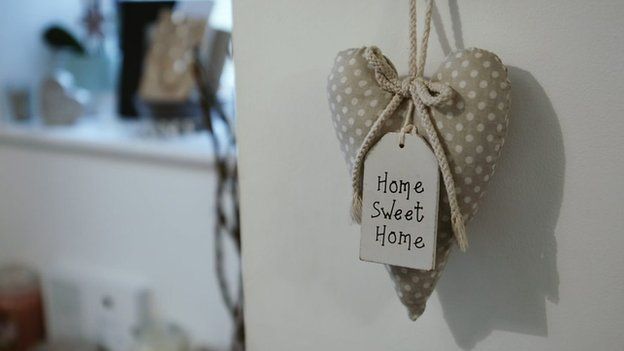 Un adorno en forma de corazón que dice hogar dulce hogar en la puerta de entrada a la casa de Alex.