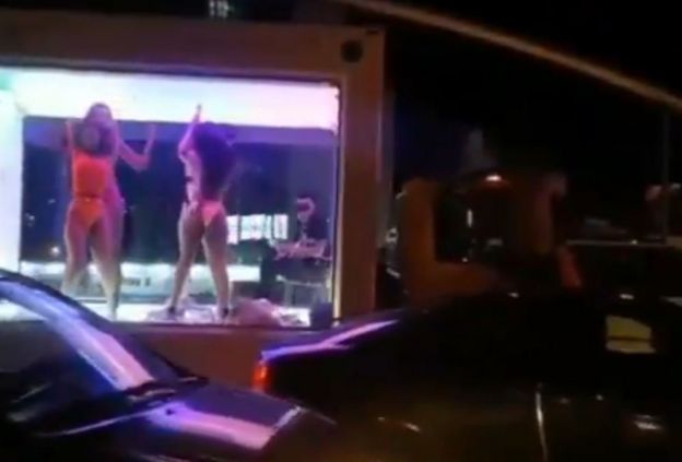 People dancing in a transparent trailer in a traffic jam