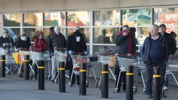 Pessoas em fila de mercado com carrinhos de compras
