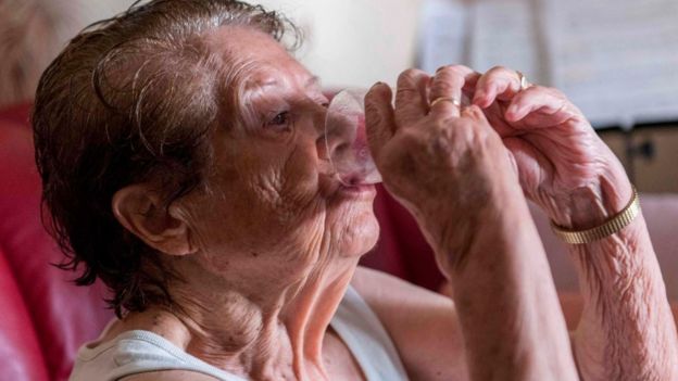 امرأة مسنة تشرب كوبا من الماء لتجنب الإصابة بضربة شمس وجفاف في وسط فرنسا