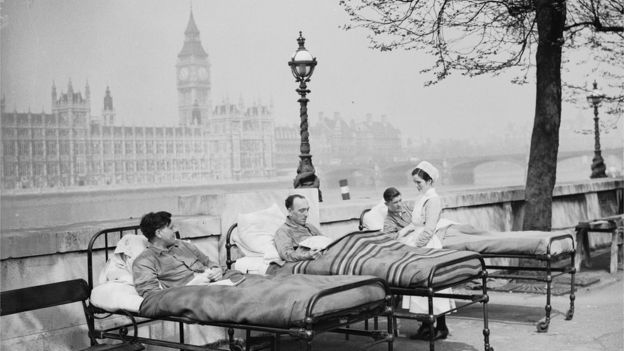 Pacientes en camas al lado del río y enfermera.