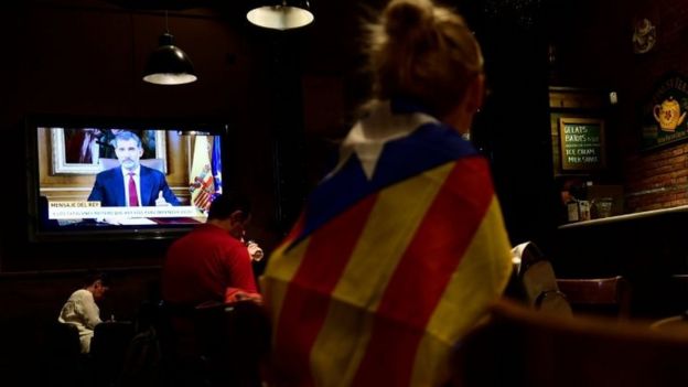 A woman wrapped in a Catalan flag listens to Spain's King Felipe VI in a bar in Barcelona. Photo: 3 October 2017