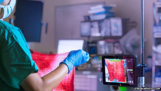 Surgeon holding up bloody cloth in front of iPad