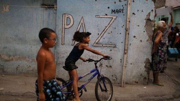 Crianças passam em frente a muro cravejado de balas