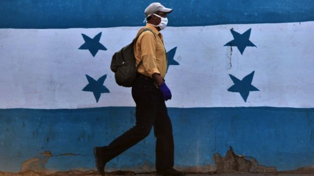 Hondureño con mascarilla ante la bandera nacional.