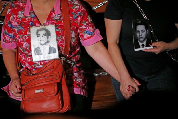 Relatives of some of the victims of Pinochet's regime hold hands while chained to church pews on 22 December