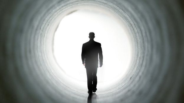 Sombra de homem caminha em direção a luz em um túnel