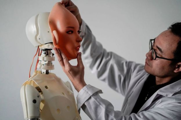 An engineer holds a silicon face against the head of a robot at a lab of a Chinese firm Exdoll